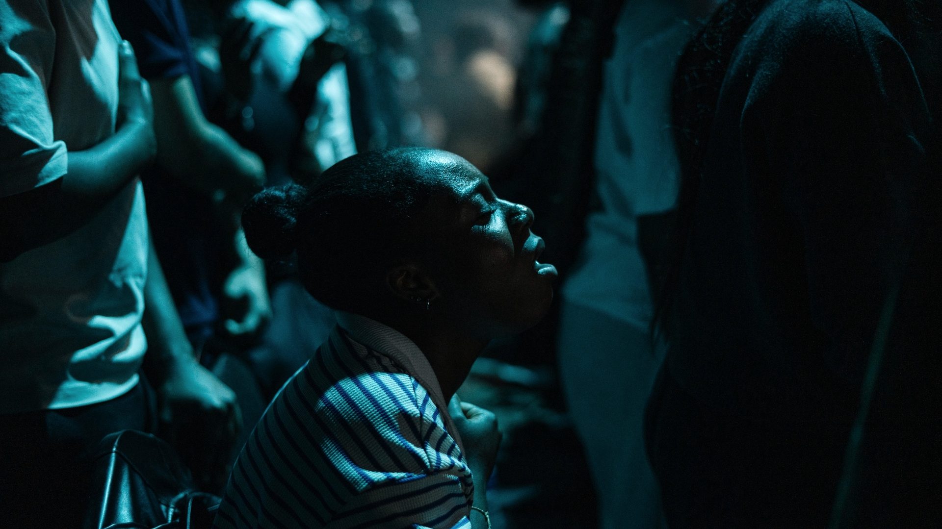 A woman kneeling in low light, face lifted in quiet prayer.